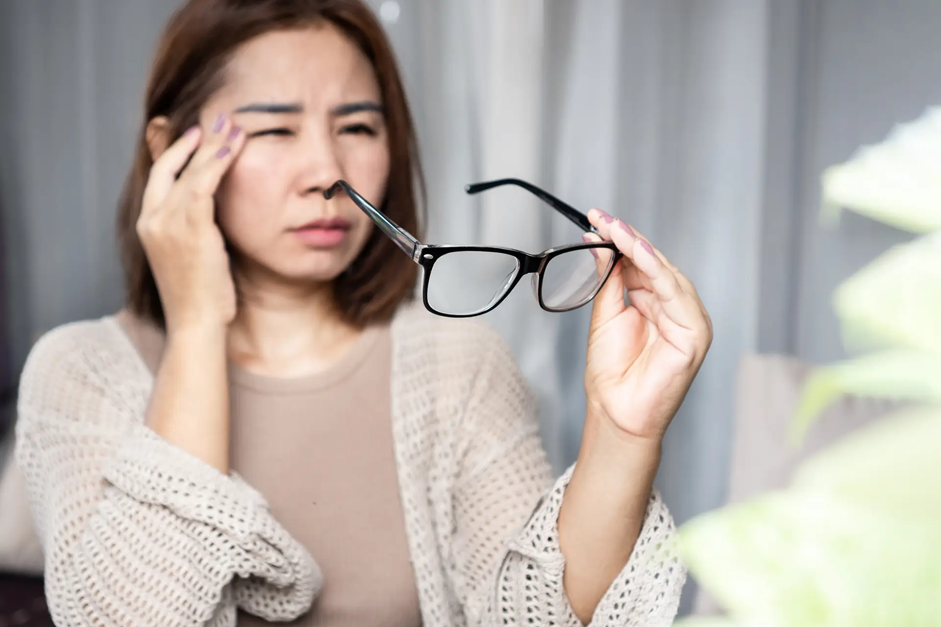 AdobeStock_1464729431 Asian woman feeling a headache, dizziness, and blurry vision while holding her eyeglasses
